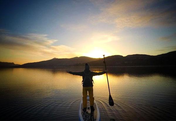 man stood on paddle board on river during sunset