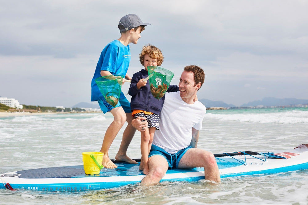 Father sitting on a paddle board with 2 sons standing around him