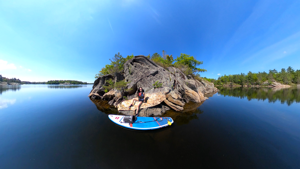 Woman sat on rocks on lake with Red Original paddling board