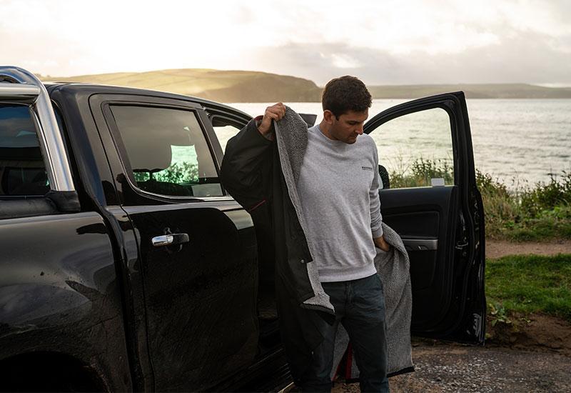 Man standing outside a pickup putting on a black waterproof changing robe