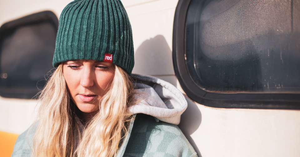 woman wearing knitted beanie in teal standing next to a caravan