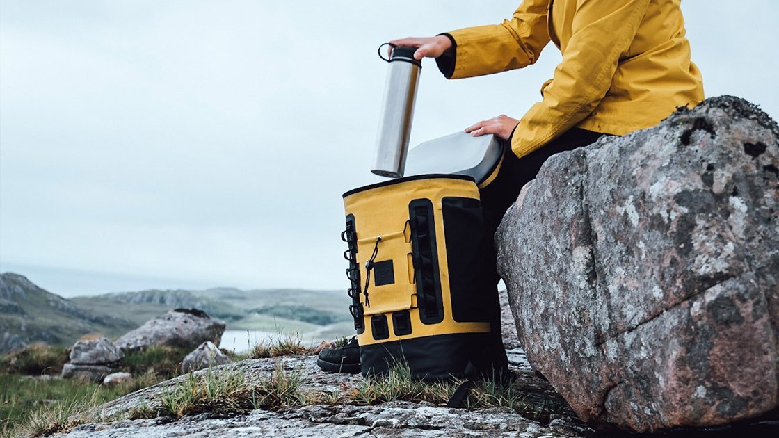 Woman Hiking taking bottle out of Mustard Backpack Cooler