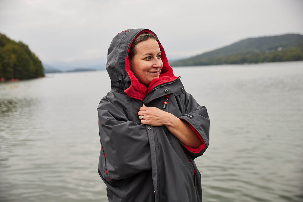 woman wrapping herself within a grey waterproof changing robe next to a lake